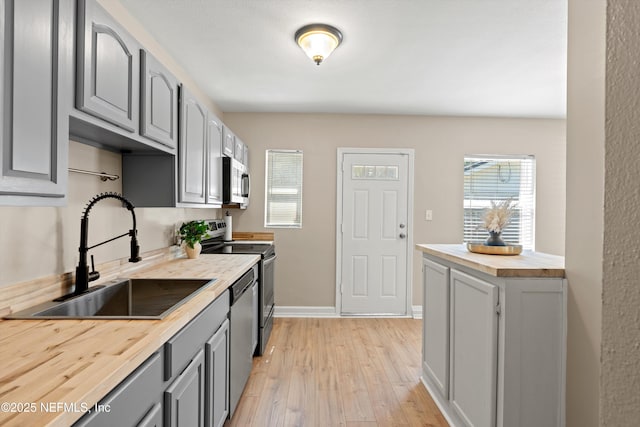 kitchen with a sink, light wood-style floors, wooden counters, appliances with stainless steel finishes, and gray cabinets