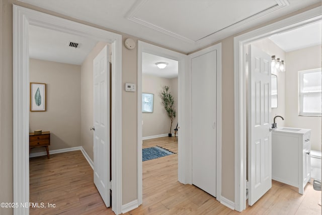 hall featuring light wood finished floors, baseboards, visible vents, and a sink