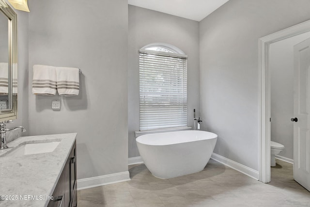 bathroom featuring toilet, a freestanding tub, baseboards, and vanity