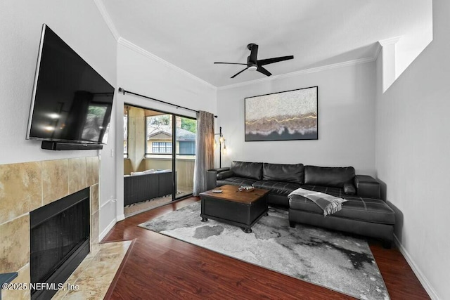 living area featuring baseboards, a tile fireplace, dark wood finished floors, and crown molding