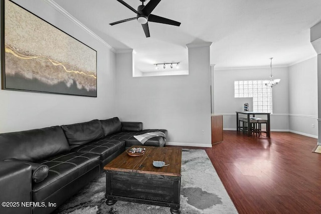 living room with ornamental molding, dark wood finished floors, baseboards, and ceiling fan with notable chandelier