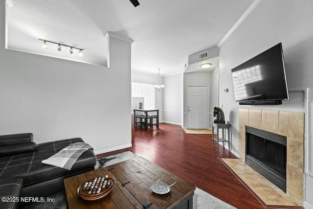 living room featuring visible vents, baseboards, dark wood-style floors, a tiled fireplace, and crown molding