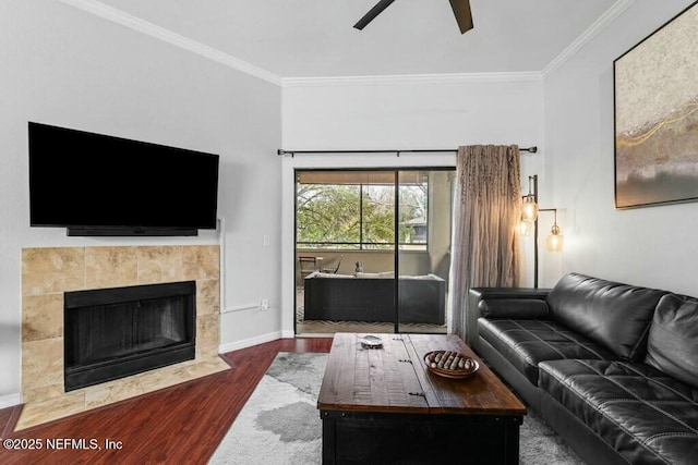 living area featuring a tiled fireplace, dark wood finished floors, a ceiling fan, and crown molding