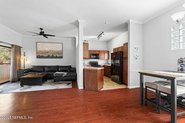 kitchen with open floor plan, wood finished floors, light countertops, crown molding, and black appliances