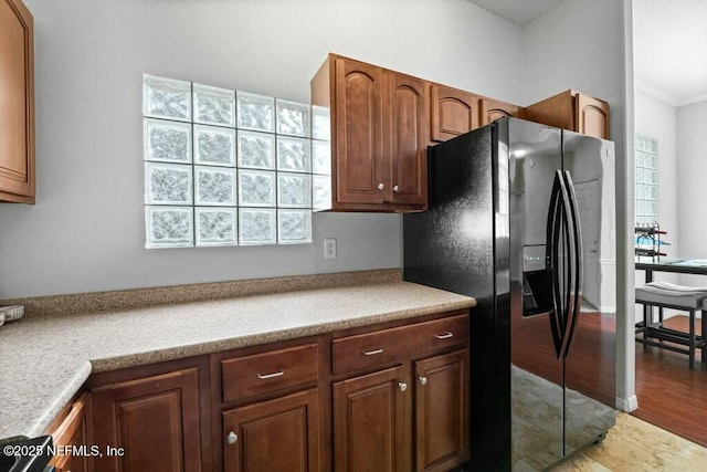 kitchen with brown cabinets, light countertops, black fridge with ice dispenser, and crown molding