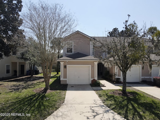 traditional home with a shingled roof, a front yard, driveway, and stucco siding