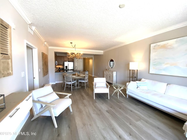 living room with a notable chandelier, crown molding, a textured ceiling, light wood-type flooring, and baseboards