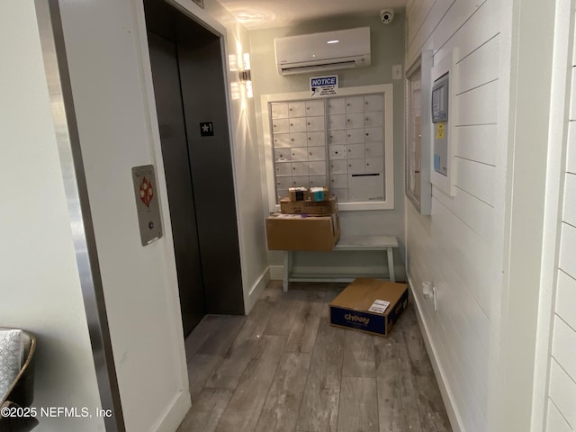 corridor with mail area, baseboards, wood finished floors, and a wall mounted AC