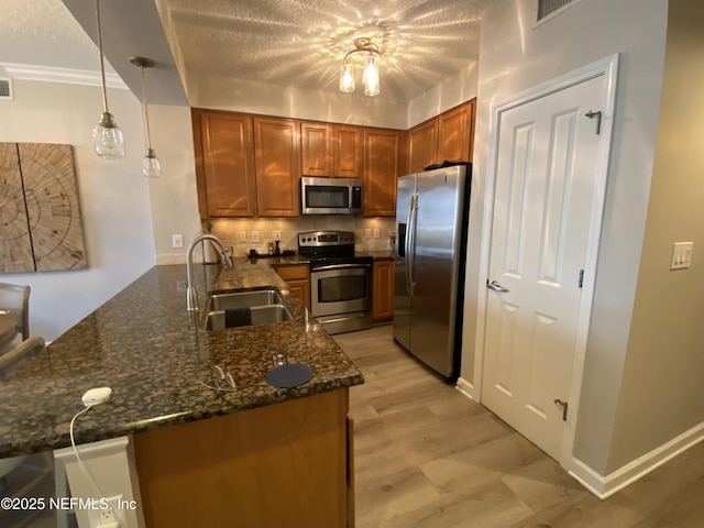 kitchen with pendant lighting, backsplash, appliances with stainless steel finishes, a sink, and a peninsula