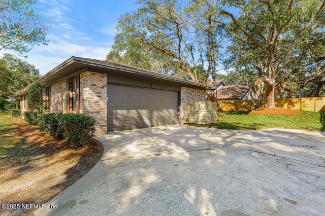 view of property exterior featuring a garage, driveway, brick siding, and fence