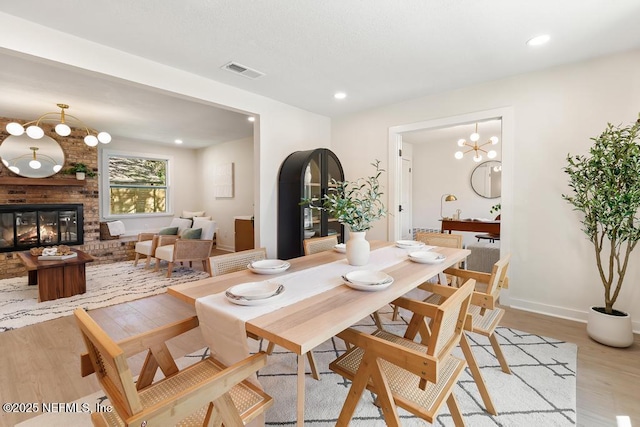 dining space featuring baseboards, visible vents, light wood-type flooring, a brick fireplace, and recessed lighting