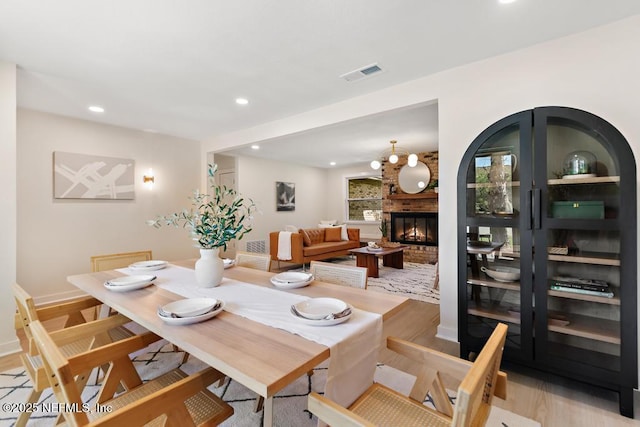 dining area featuring light wood-type flooring, recessed lighting, visible vents, and a fireplace