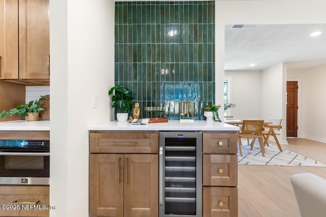 bar with a dry bar, visible vents, light wood-style flooring, wine cooler, and oven