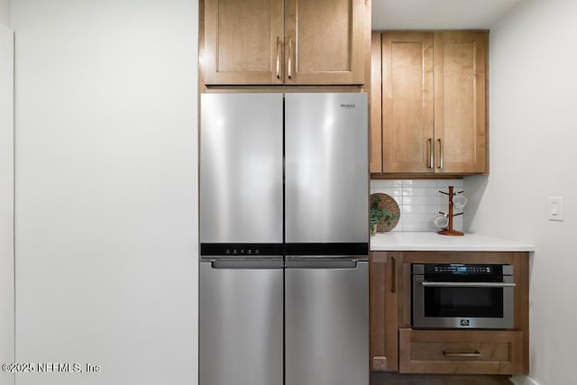 kitchen with stainless steel appliances, tasteful backsplash, light countertops, and brown cabinets