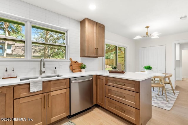 kitchen with a peninsula, stainless steel dishwasher, a sink, and light countertops