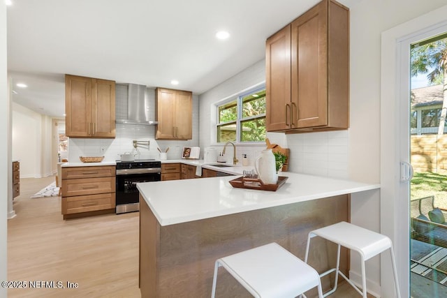 kitchen featuring a peninsula, range with electric cooktop, a sink, wall chimney range hood, and decorative backsplash