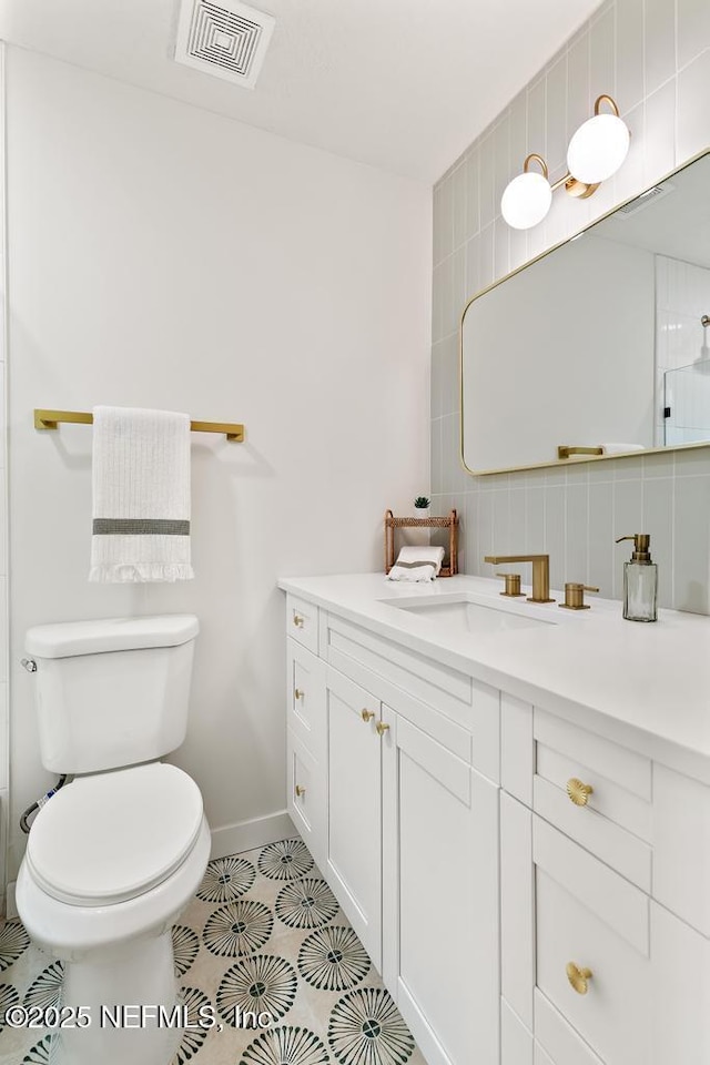 bathroom with baseboards, visible vents, decorative backsplash, toilet, and vanity