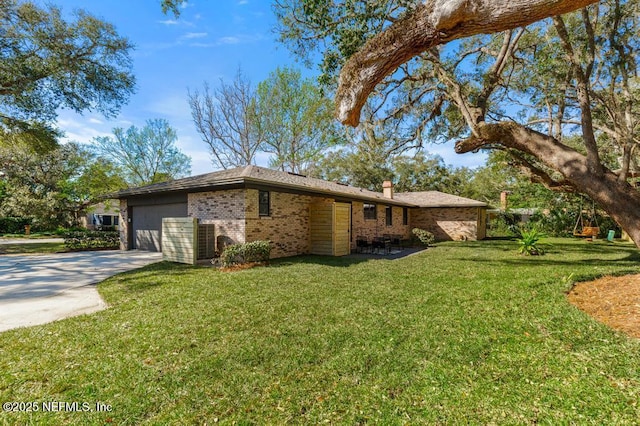 view of side of home featuring a garage, concrete driveway, a chimney, a yard, and brick siding