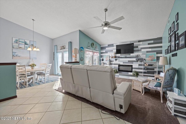 living area featuring lofted ceiling, an accent wall, light tile patterned flooring, a textured ceiling, and ceiling fan with notable chandelier