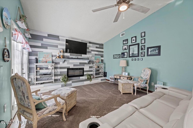 carpeted living area with lofted ceiling, visible vents, an accent wall, a glass covered fireplace, and a textured ceiling