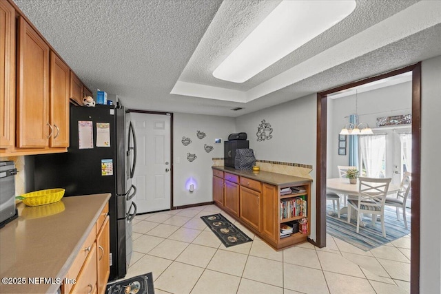 kitchen featuring brown cabinets, freestanding refrigerator, light tile patterned flooring, a textured ceiling, and baseboards