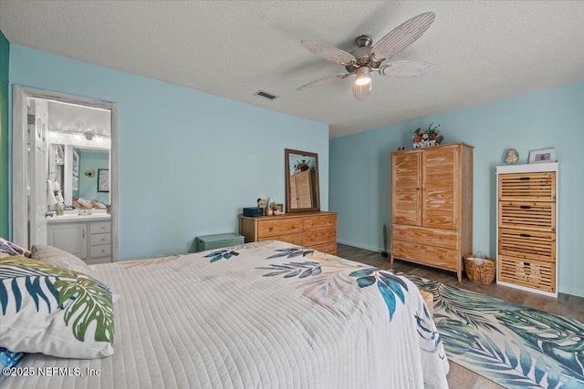 bedroom with a textured ceiling, wood finished floors, visible vents, and ensuite bathroom