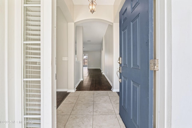 foyer entrance with light tile patterned floors, arched walkways, and baseboards