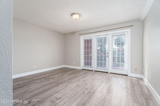 spare room featuring light wood-type flooring, baseboards, and a textured ceiling