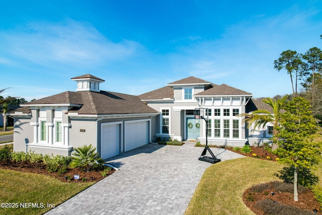 prairie-style house featuring a garage, roof with shingles, decorative driveway, a front lawn, and stucco siding