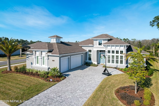 prairie-style home with a garage, a front yard, decorative driveway, and stucco siding