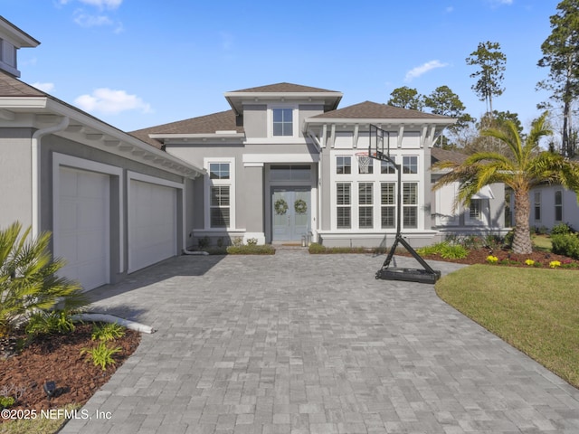 prairie-style house featuring an attached garage, stucco siding, decorative driveway, and french doors