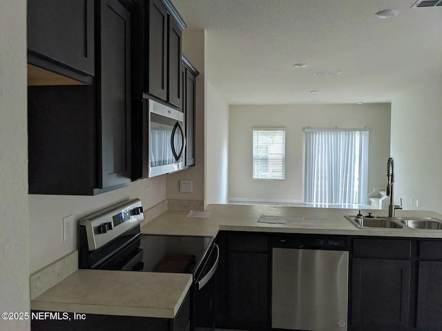 kitchen with appliances with stainless steel finishes, light countertops, a sink, and dark cabinets