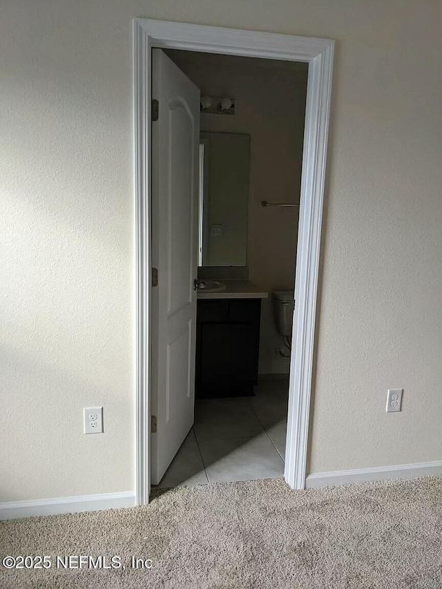 hallway with a textured wall, light tile patterned flooring, light carpet, a sink, and baseboards