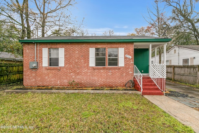 view of front of house with covered porch, brick siding, a front yard, and fence