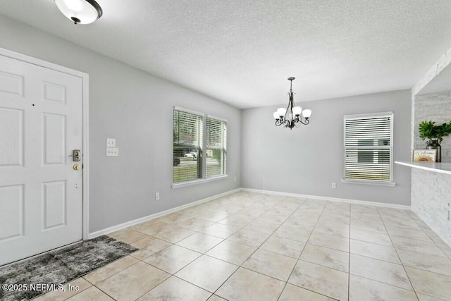 entrance foyer featuring a chandelier, light tile patterned floors, a textured ceiling, and baseboards