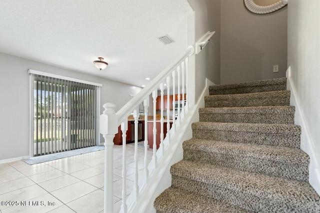 stairway with tile patterned flooring, visible vents, and baseboards