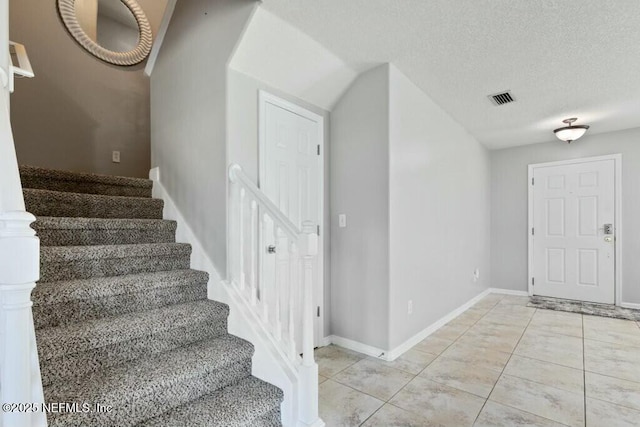 staircase featuring tile patterned flooring, baseboards, visible vents, and a textured ceiling