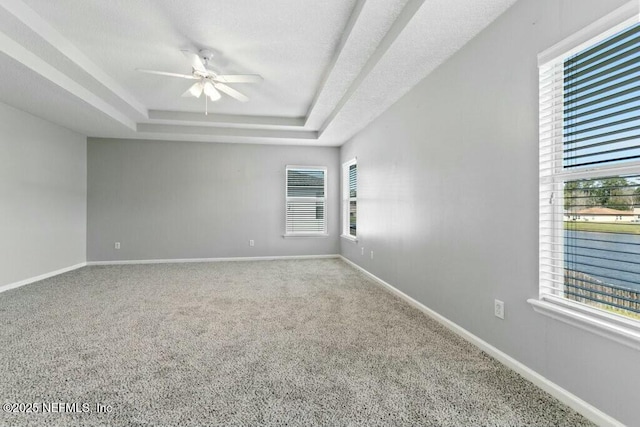 carpeted spare room featuring ceiling fan, baseboards, and a raised ceiling