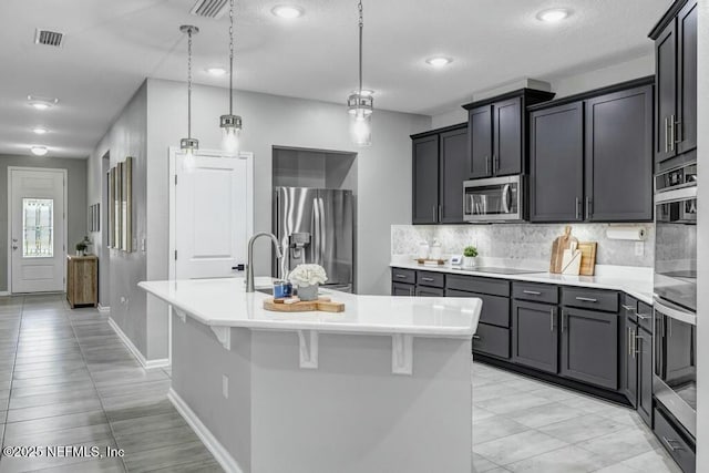 kitchen featuring appliances with stainless steel finishes, light countertops, backsplash, and an island with sink