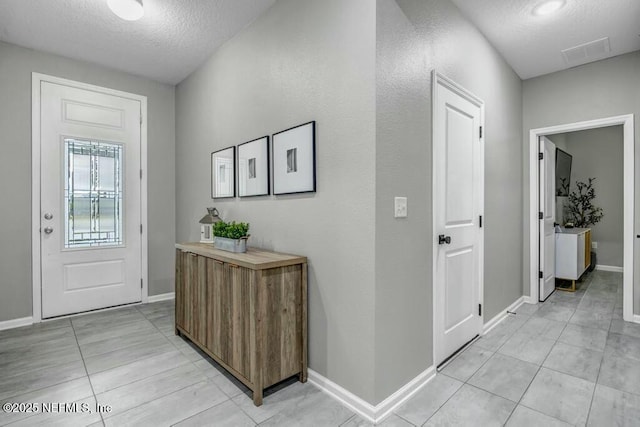 foyer entrance with a textured ceiling, light tile patterned floors, visible vents, and baseboards