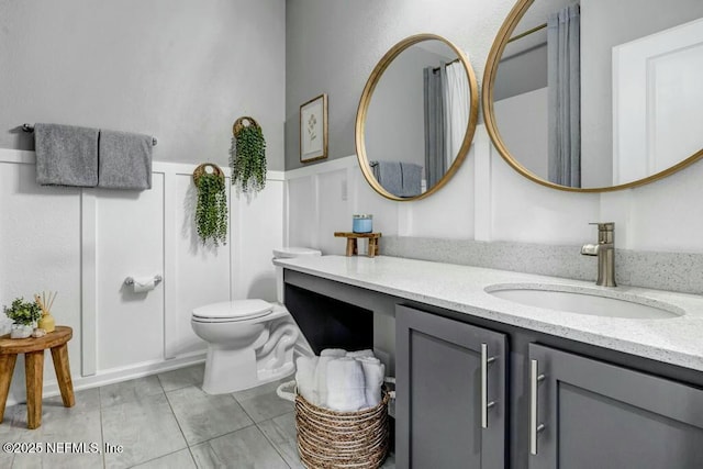 bathroom with a wainscoted wall, a decorative wall, vanity, and toilet