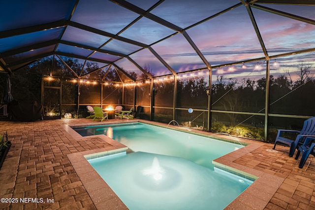 pool at dusk with a patio, an outdoor fire pit, and glass enclosure