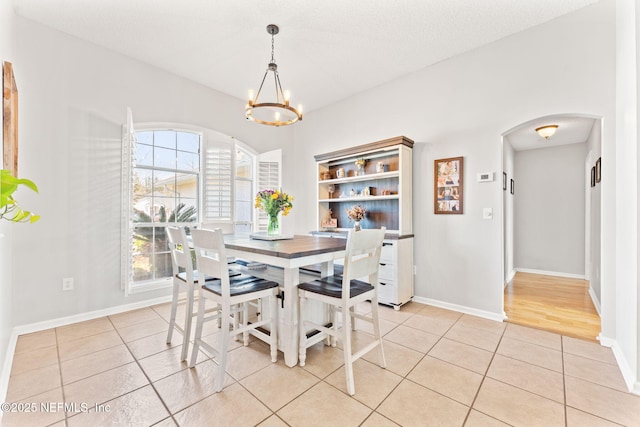 dining area with arched walkways, a textured ceiling, a chandelier, light tile patterned flooring, and baseboards