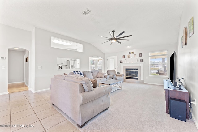 living area with arched walkways, ceiling fan, lofted ceiling, a tile fireplace, and visible vents