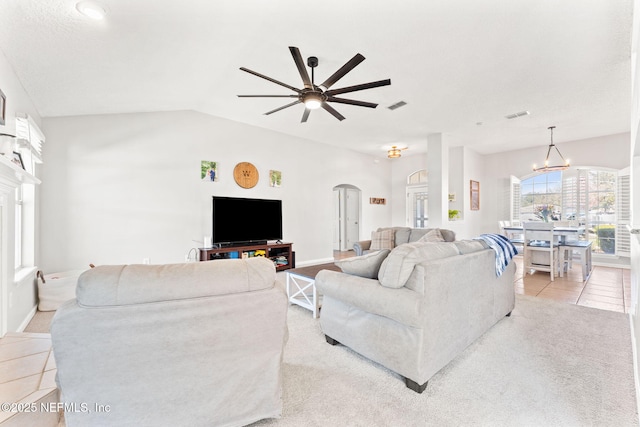 living area with arched walkways, light tile patterned floors, visible vents, vaulted ceiling, and ceiling fan with notable chandelier