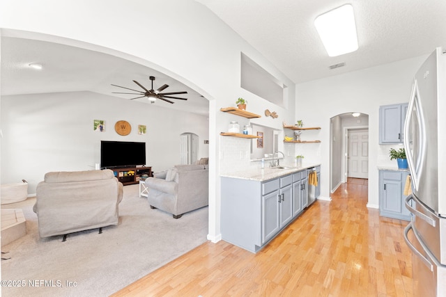 kitchen featuring visible vents, arched walkways, freestanding refrigerator, vaulted ceiling, and open shelves