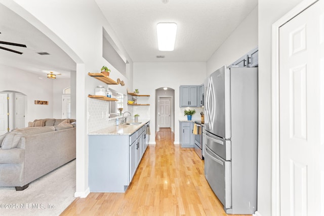 kitchen with arched walkways, open floor plan, stainless steel appliances, open shelves, and a sink