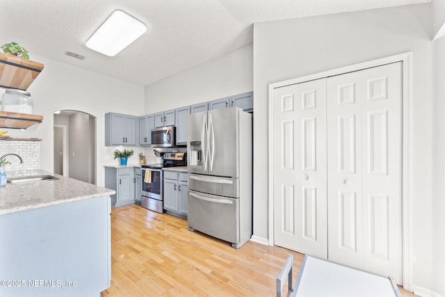 kitchen with arched walkways, stainless steel appliances, a sink, light wood-type flooring, and open shelves