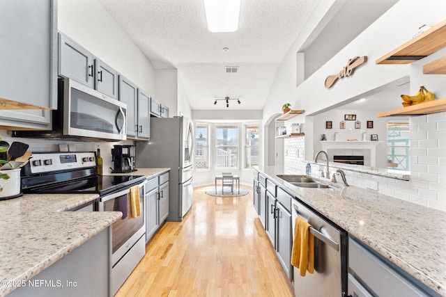 kitchen with a tile fireplace, appliances with stainless steel finishes, gray cabinetry, light wood-type flooring, and a sink