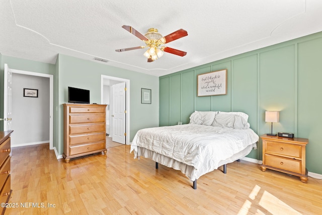 bedroom with light wood finished floors, visible vents, ceiling fan, a textured ceiling, and a decorative wall